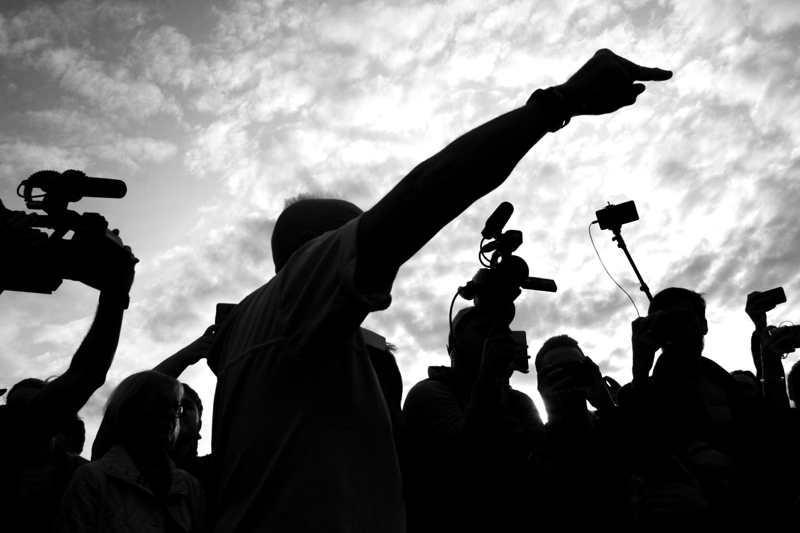 Manifestante gesticula enquanto câmeras e smartphones registram o momento. Foto: Nikita Kotrelev no Pexels