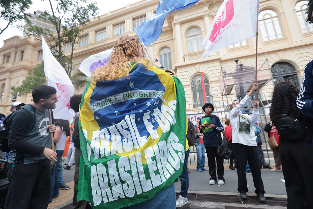 Manifestante com bandeira do Brasil nas costas, onde se lê “Brasil é dos brasileiros”, participa de ato do 7 de Setembro na Praça da República, em São Paulo. Outras pessoas seguram bandeiras de movimentos sociais, como a da UJS. Praça da República, São Paulo (SP), 07/09/2025. Foto: Paulo Pinto / Agência Brasil