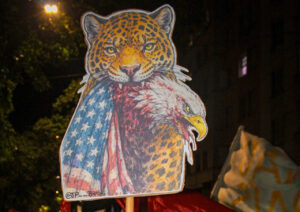 Manifestante em marcha antifascista em Porto Alegre segura cartaz com símbolo crítico ao imperialismo durante conferência internacional. Ryan Rodrigues – Marcha da Conferência Internacional Antifascista pela soberania dos povos, Porto Alegre, março de 2026.